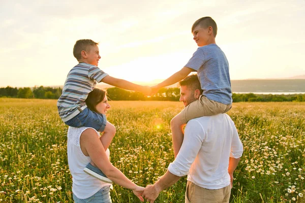 Famiglia felice sul campo margherita al tramonto divertendosi insieme — Foto Stock