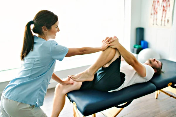 밝은 사무실에서 다리 훈련을 받은 환자와 함께 치료하는 물리 치료사 — 스톡 사진