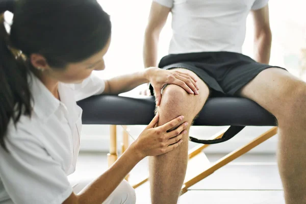 Физиотерапевт делает лечение с пациентом в ярком офисе проверить колено — стоковое фото