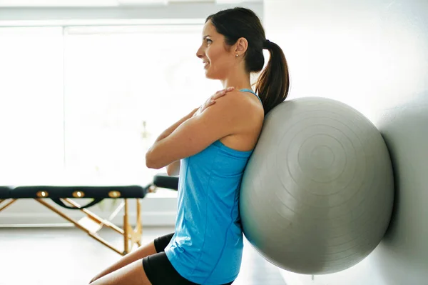 Молодая женщина делает упражнения на фитнес-мяч в кабинете физиотерапии — стоковое фото