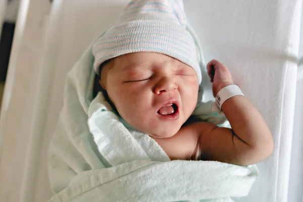 Новонароджена дитина спить, одягнена в лікарняну ковдру і носить капелюх — стокове фото