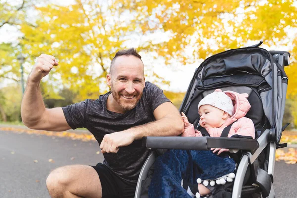 Чоловік зі своєю дочкою стоїть у колясці для бігу надворі восени — стокове фото