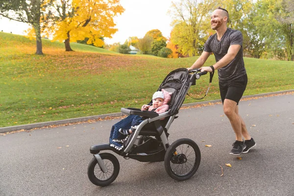 Чоловік зі своєю дочкою в колясці для бігу зовні в осінній характер — стокове фото
