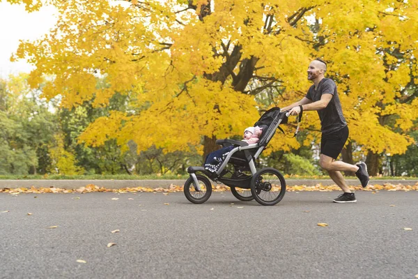 Man with her daughter in jogging stroller outside in autumn nature — Stock Photo, Image