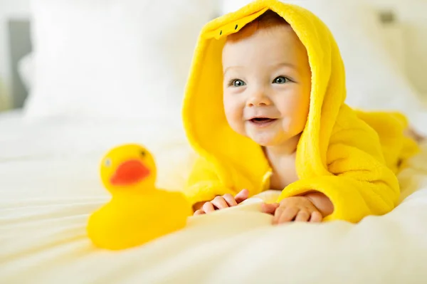 Bebé usando pato de albornoz amarillo en la cama de los padres después del baño — Foto de Stock