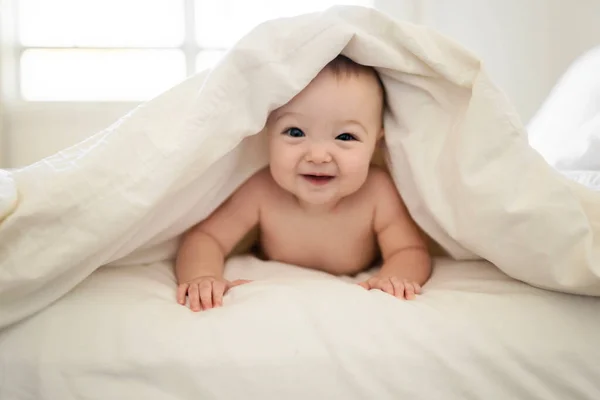 Retrato de un bebé bajo una manta en la cama en el dormitorio de los padres — Foto de Stock