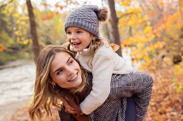 Kleines Mädchen und ihre Mutter spielen im Herbstpark mit Kind auf dem Rücken — Stockfoto