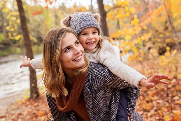 Klein meisje en haar moeder spelen in de herfst park met kind op de rug — Stockfoto