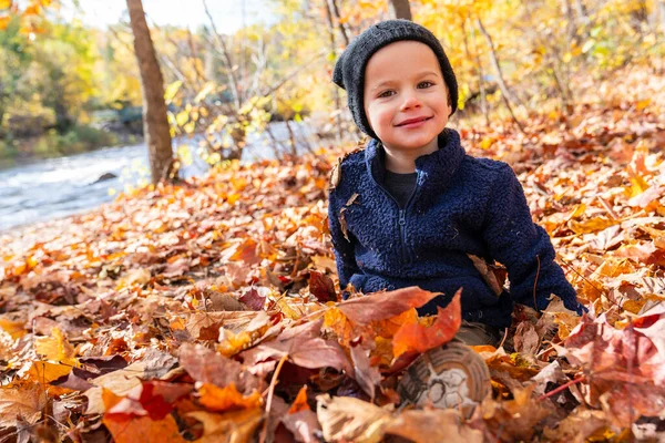 가을에는 귀여운 소년이 나뭇잎 위에 앉아 있다 — 스톡 사진