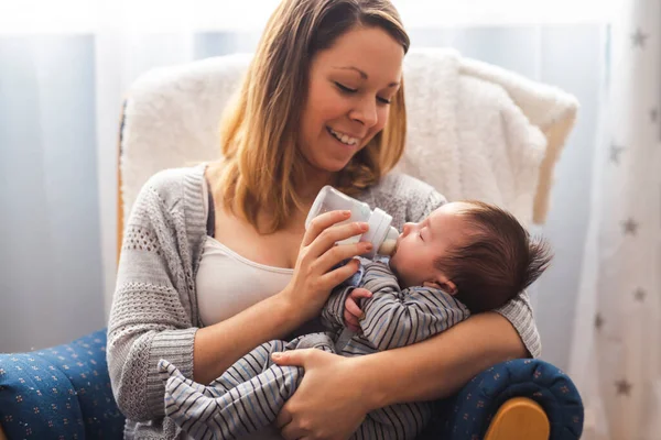 Retrato de una bonita madre alimentando a su bebé recién nacido de un biberón mientras se relaja en casa — Foto de Stock