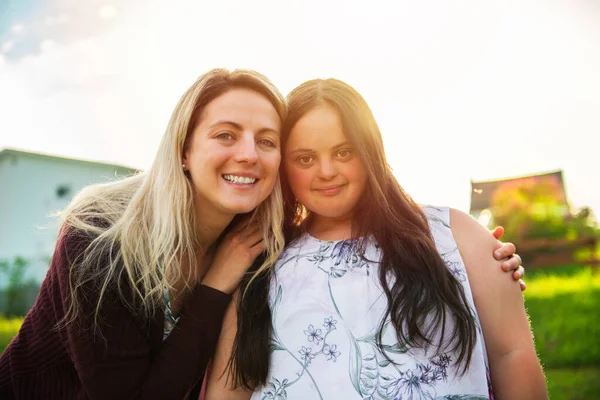 Um retrato de trissomia 21 menina adulta sorrir fora ao pôr do sol com o amigo da família — Fotografia de Stock