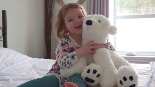 Симпатична маленька дівчинка в піжамі обіймає свого іграшкового зайця на ліжку вдома — стокове відео