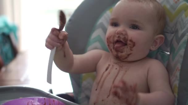 Een portret van gelukkig jong meisje in kinderstoel eten chocolade — Stockvideo