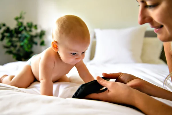 Um retrato de um bebê bonito verificando smartphone deitado em uma cama — Fotografia de Stock