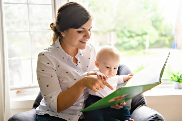 幸せな家族だ。かなり若い母親が赤ちゃんに本を読んで — ストック写真