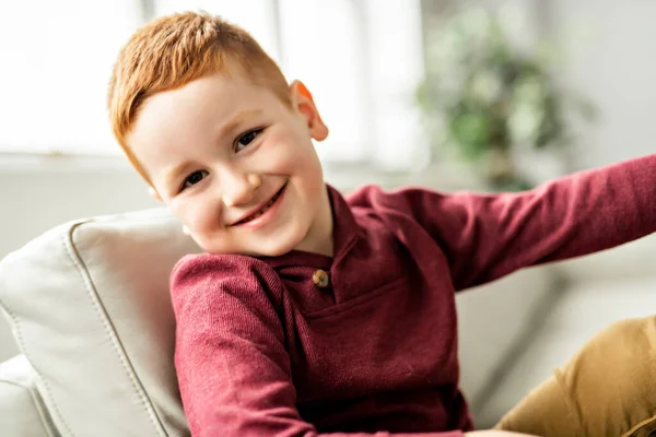 Симпатичный рыжий мальчик сидит дома на диване. — стоковое фото