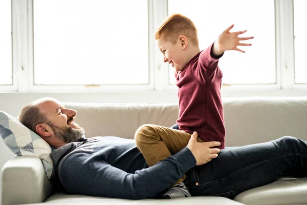 Ojciec z rudym dzieckiem bawiący się na kanapie w domu — Zdjęcie stockowe