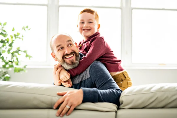 赤い頭の子供を持つ父はソファの上に家に座って — ストック写真