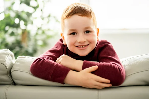 Рыжий ребенок сидит дома на диване — стоковое фото
