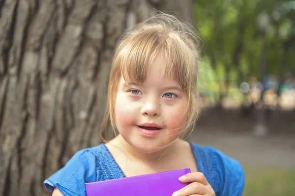 Portrét trisomie 21 dítě dívka venku baví v parku čtení knihy — Stock fotografie