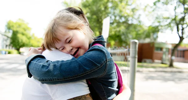 A portrait of trisomie 21 child girl outside hugging his mother on a school playground — Stock Photo, Image