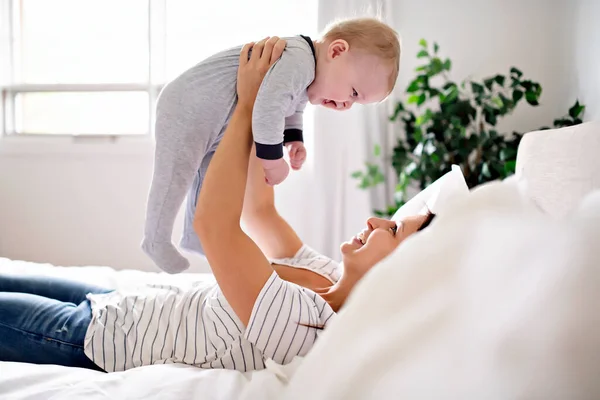 Mãe e criança em uma cama branca brincando no quarto ensolarado — Fotografia de Stock