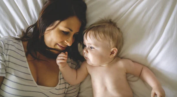 Mother and child on a white bed playing in sunny bedroom — Stock Photo, Image