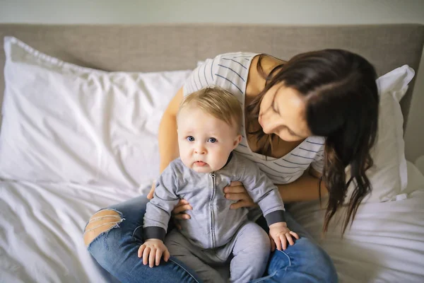 Madre e hijo en una cama blanca jugando en el dormitorio soleado — Foto de Stock