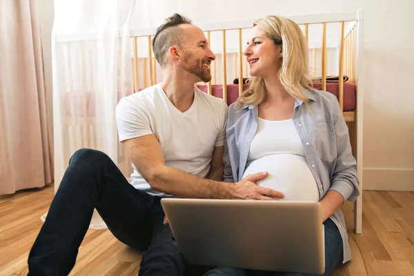 Ευτυχισμένος άνθρωπος και η έγκυος γυναίκα του με υπολογιστή στο δωμάτιο του μωρού στο σπίτι — Φωτογραφία Αρχείου