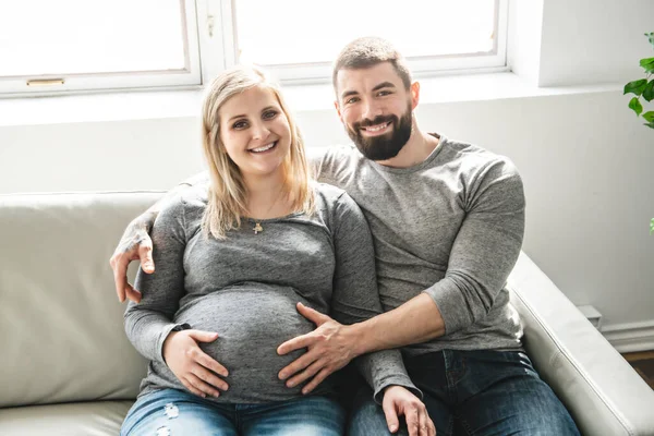 Un uomo che abbraccia una donna incinta felice seduta sul divano — Foto Stock