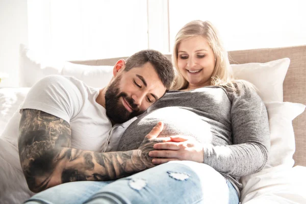 L'uomo appoggiato al pancione della moglie incinta che giace sul letto — Foto Stock