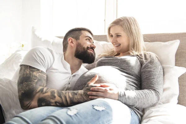 De man leunde tegen de baby hobbel van zijn zwangere vrouw, die ligt op het bed — Stockfoto