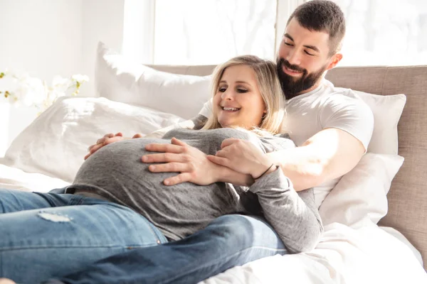 De man leunde tegen de baby hobbel van zijn zwangere vrouw, die ligt op het bed — Stockfoto