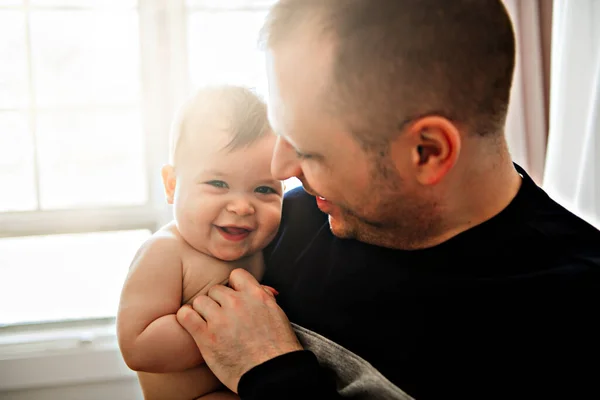 Um jovem pai com um bebê em um belo quarto com janela nas costas — Fotografia de Stock