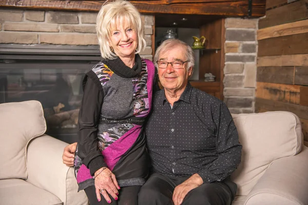 Romántica pareja de ancianos sentados juntos en un sofá en la casa sonriendo felizmente a la cámara — Foto de Stock