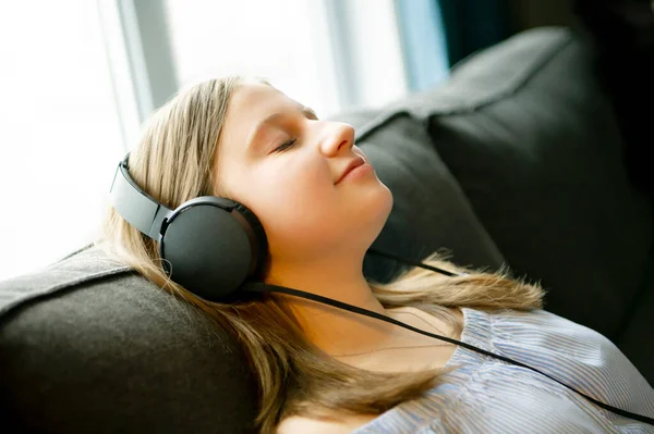 Meisje luisteren muziek met koptelefoon liggend op de bank thuis — Stockfoto