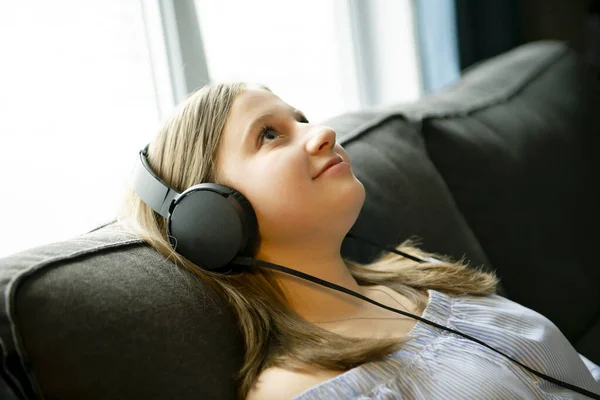 Girl listening music with headphones lying on couch at home — ストック写真