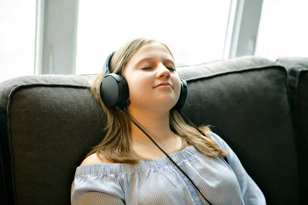 Ragazza che ascolta musica con le cuffie sdraiato sul divano a casa — Foto Stock