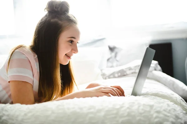 Une jeune adolescente souriante sur le lit avec ordinateur portable — Photo