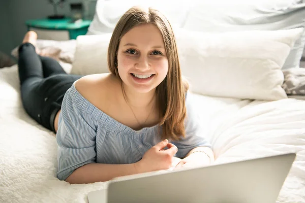 Молода усміхнена дівчина-підліток на ліжку з ноутбуком — стокове фото
