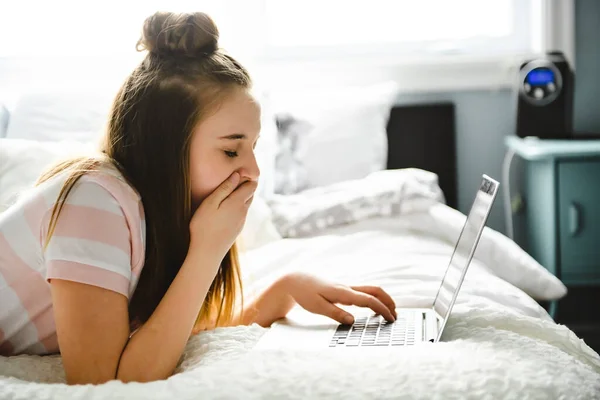 Молода усміхнена дівчина-підліток на ліжку з ноутбуком — стокове фото
