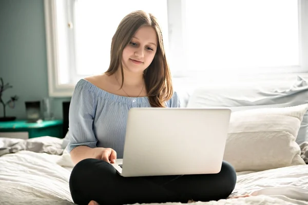 Een jong lachend tiener meisje op bed met laptop — Stockfoto