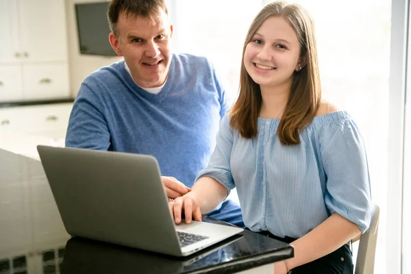 Um pai usando um laptop na cozinha com adolescente — Fotografia de Stock