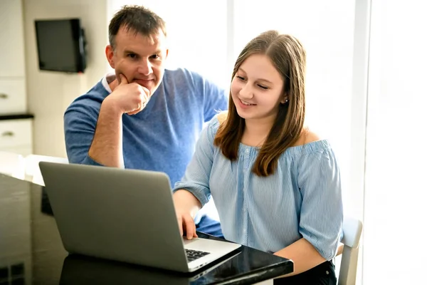 En far som använder en laptop i köket med tonåring — Stockfoto