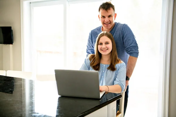 Um pai usando um laptop na cozinha com adolescente — Fotografia de Stock