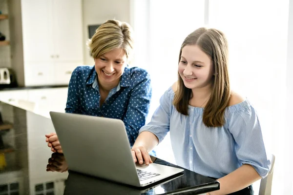 En mamma som använder en laptop i köket med tonåring — Stockfoto