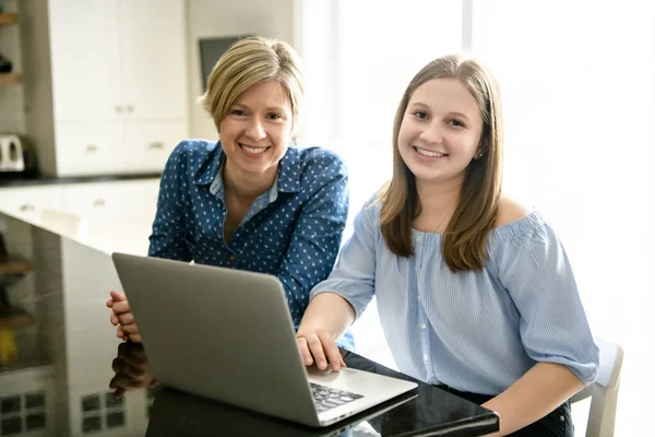 Uma mãe usando um laptop na cozinha com adolescente — Fotografia de Stock