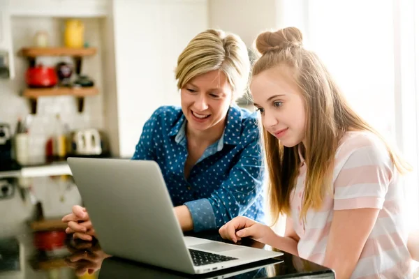 Uma mãe usando um laptop na cozinha com adolescente — Fotografia de Stock