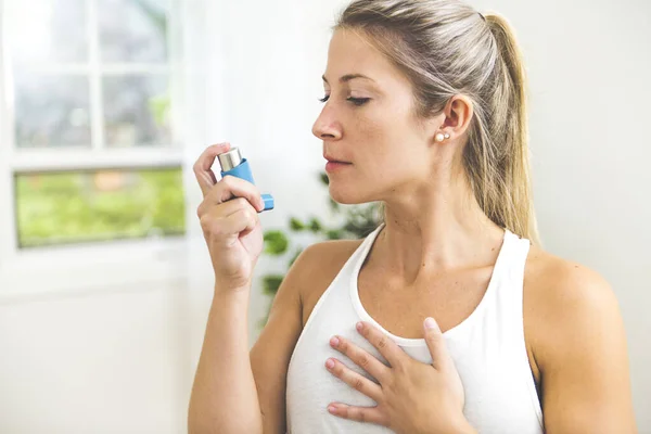 Una mujer joven que usa inhalador de asma en casa —  Fotos de Stock