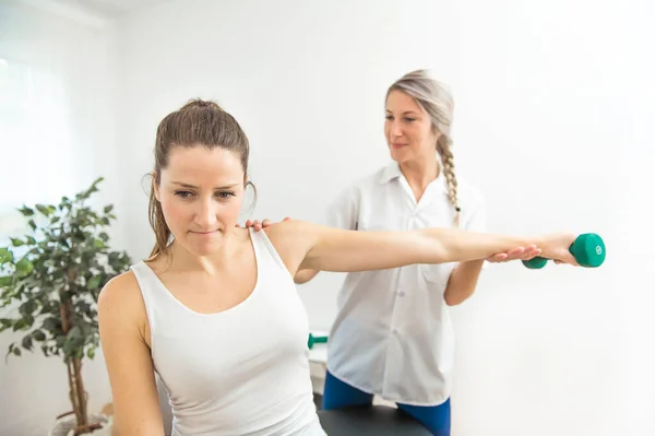 Um fisioterapeuta de reabilitação moderna no trabalho com o cliente. Trabalhando no ombro com halteres — Fotografia de Stock